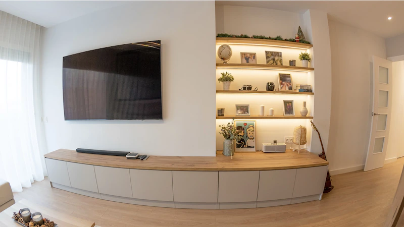 Mueble de televisión a medida con larga bancada baja en madera de roble y puertas visón mate con hornacina empotrada e iluminación LED cálida en Barcelona por Fustaire