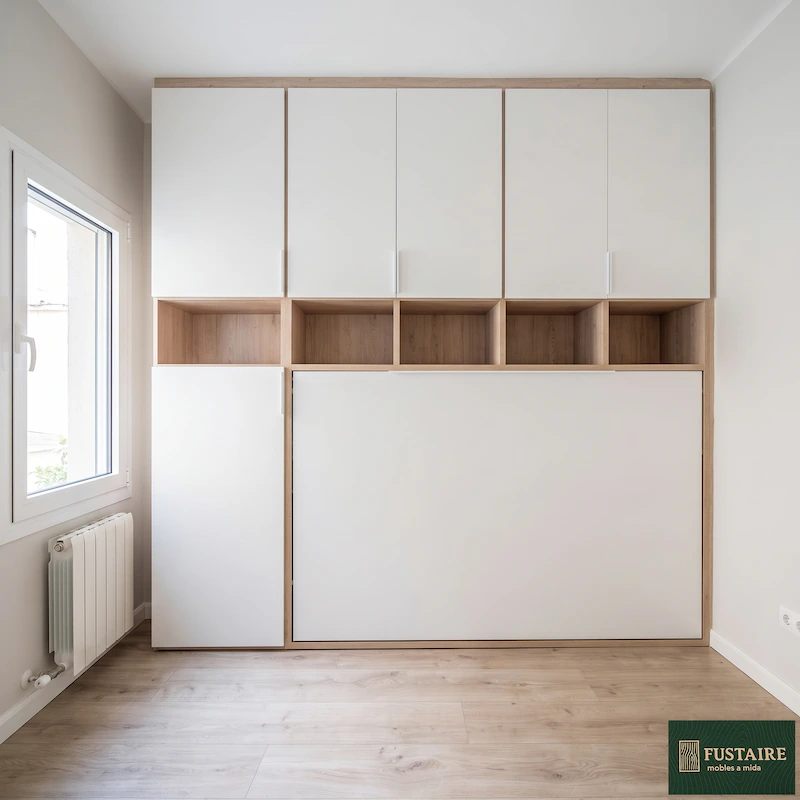 Armario multifuncional moderno con cama abatible integrada, diseñado en color blanco mate y madera clara. Un proyecto de carpintería para optimizar el espacio en un dormitorio, fabricado como mueble a medida en Barcelona por Fustaire.