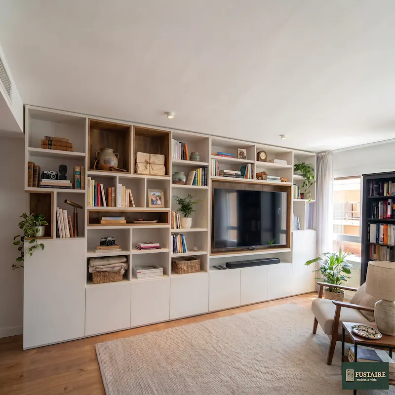 Gran mueble mural de salón comedor a medida de pared a pared con librería en blanco, hornacinas en madera de nogal y espacio de televisión integrado en Barcelona por Fustaire Mobles a Mida